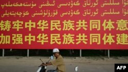 一名骑电摩托的男子路过新疆喀什莎车县的一面政府竖立的宣传牌。(2023年7月17日)