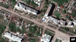 This satellite image provided by Maxar Technologies shows a Russian armor unit deployed along a road and the aftermath of artillery bombardments with destroyed buildings, in Popasna, a town in Sievierodonetsk Raion, Ukraine, Wednesday, May 25, 2022. (Sate