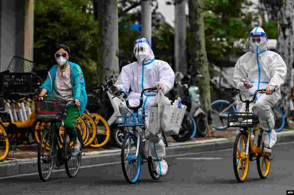 Workers wearing personal protective equipment (PPE) cycle on a street during a Covid-19 coronavirus lockdown in the Jing&#39;an district of Shanghai, China.