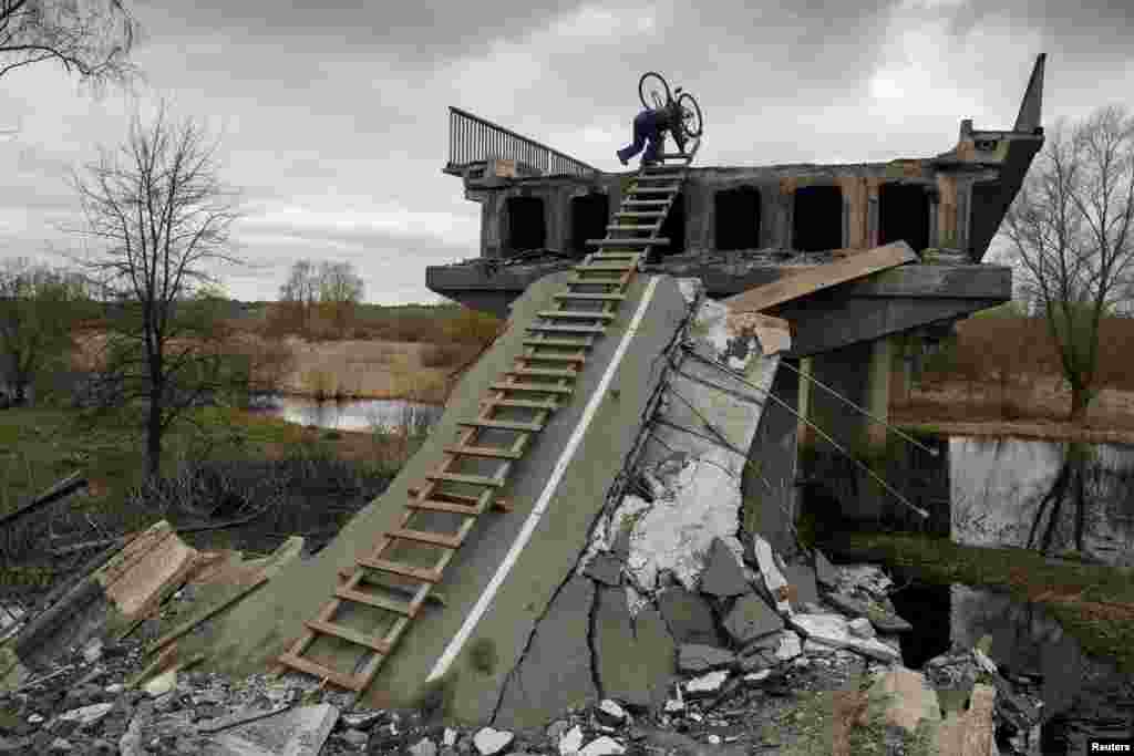 A local resident Mykola, 70, climbs down with a bicycle from a bridge destroyed during Russia&#39;s invasion in the village of Kukhari in Kyiv region, Ukraine, April 19, 2022.