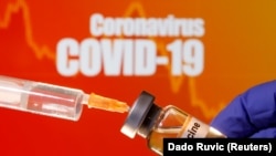 FILE PHOTO: A small bottle labeled with a "Vaccine" sticker is held near a medical syringe in front of displayed "Coronavirus COVID-19" words in this illustration taken April 10, 2020.