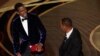 Presenter Chris Rock, left, reacts after being hit on stage by Will Smith while presenting the award for best documentary feature at the Oscars on Sunday, March 27, 2022