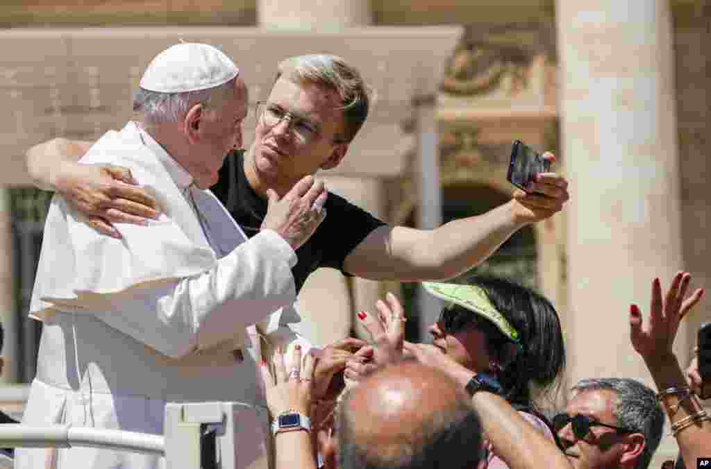 A man hugs Pope Francis to take a selfie after he had climbed on the popemobile at the end of the weekly general audience in St. Peter&#39;s Square at the Vatican.