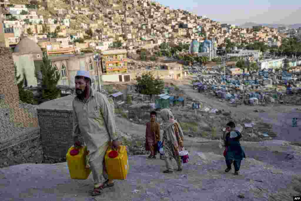 People carry drinking water in containers near the Kart-e-Sakhi cemetery in Kabul, Afghanistan.