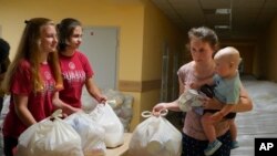 A woman carries her child as she receives humanitarian aid provided by local authorities in Selidovo, Donetsk region, Ukraine, Tuesday, June 14, 2022.