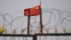 资料照片：中国国旗在新疆喀什南部地区一处建筑物的围栏铁丝网后飘扬。（2019年6月4日）