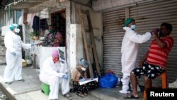 A health worker collects a nasal swab sample of a resident to test for test for COVID-19 in a slum area in Mumbai, India, Sept. 5, 2020.