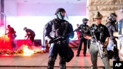 Law enforcement officers stand watch and extinguish a fire set by protesters behind the Mark O. Hatfield United States Courthouse in Portland.