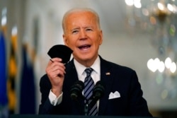 President Joe Biden holds up his face mask as he speaks about the COVID-19 pandemic during a prime-time address from the East Room of the White House, March 11, 2021.